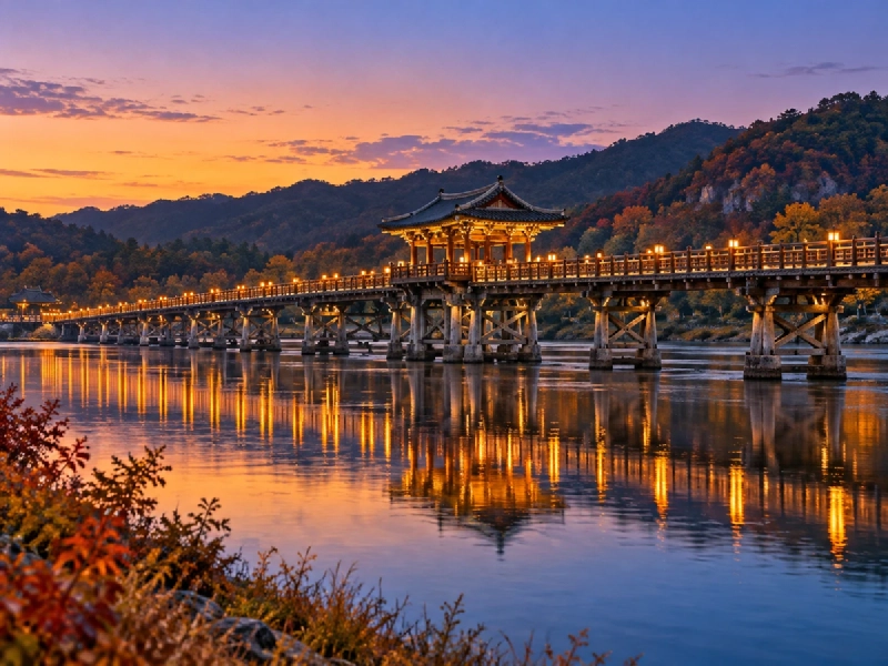 夕暮れの川に架かる長い木造の橋が、柔らかな灯りに照らされて水面に映る風景