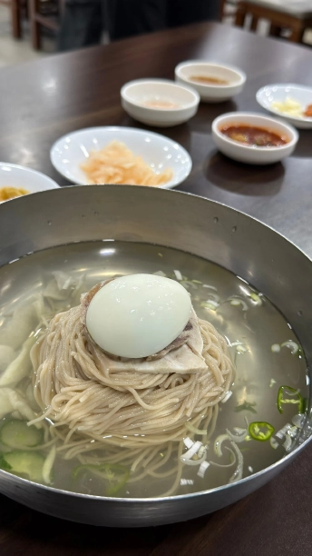 ステンレスの器に盛られた平壌冷麺。澄んだスープにゆで卵、肉、きゅうり、大根がのっている