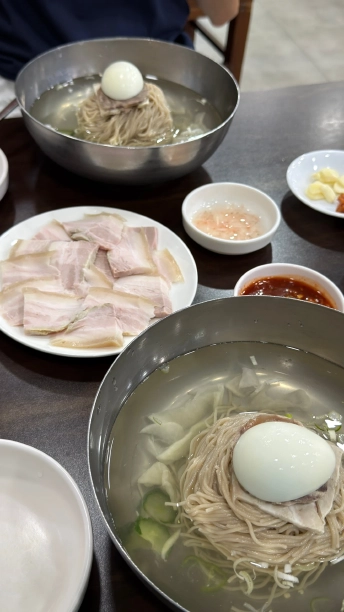 平壌冷麺2杯と、薄切りのゆで豚の皿、赤いタレや薬味が並んだテーブル