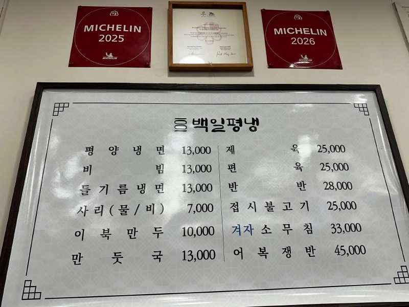 ペギルピョンネンの店内の壁。MICHELIN 2025と2026の赤いプレート、選出を伝える額、ハングルのメニュー板が並ぶ