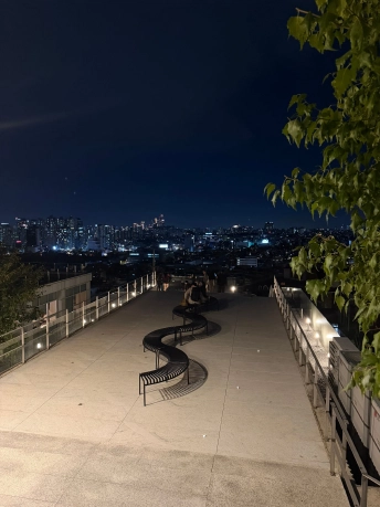 波形のベンチが並ぶコンフォートの屋上テラスと、ソウル市街の夜景