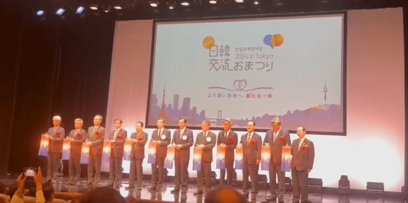 「日韓交流おまつり 2026 in Tokyo」のロゴが映るスクリーンの前で、提灯を手にした関係者がステージに並ぶ点灯式