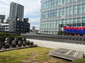 芝生の庭に甕が並び、瓦屋根の塀の向こうに高層ビルが見える屋上
