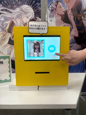 黄色い筐体の画面に、キャラクターのフレームに囲まれた人物が映るレシート写真機