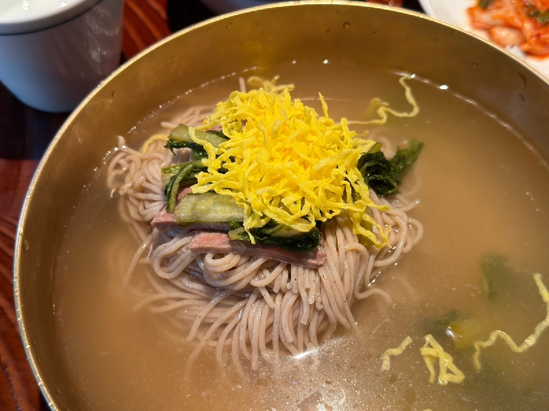 真鍮色の器に盛られた平壌冷麺。錦糸卵と牛肉、青菜がのっている