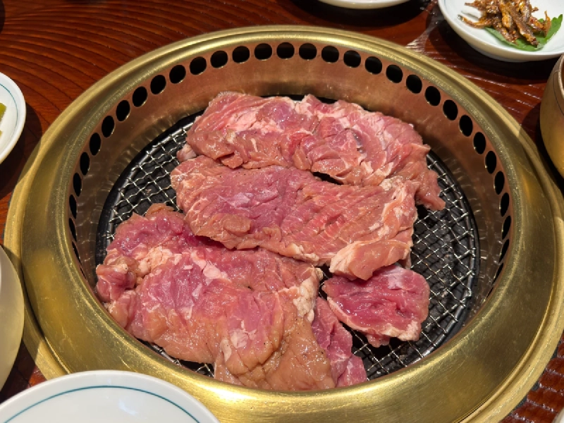 炭火の網にのせた焼く前の豚カルビ。厚みのある肉が並ぶ