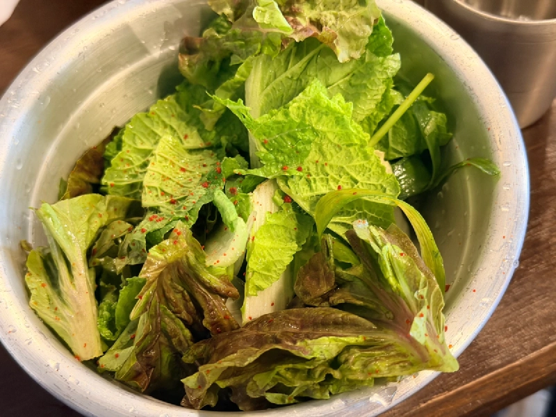 唐辛子粉をふったサンチュなどの葉野菜が入った金属のボウル